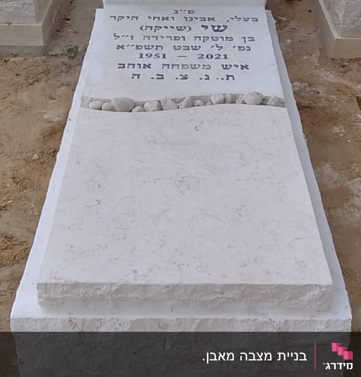 מצבה לבנה עם כיתוב בעברית ואבנים קטנות